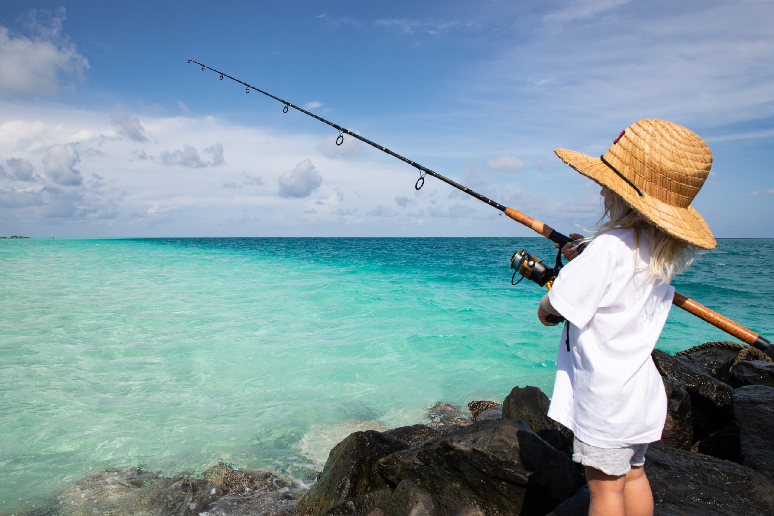 A small child fishes off the rocks into clear tropical water on vacation